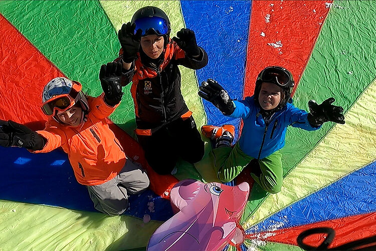 Kinder mit Skilehrer auf Spielfallschirm